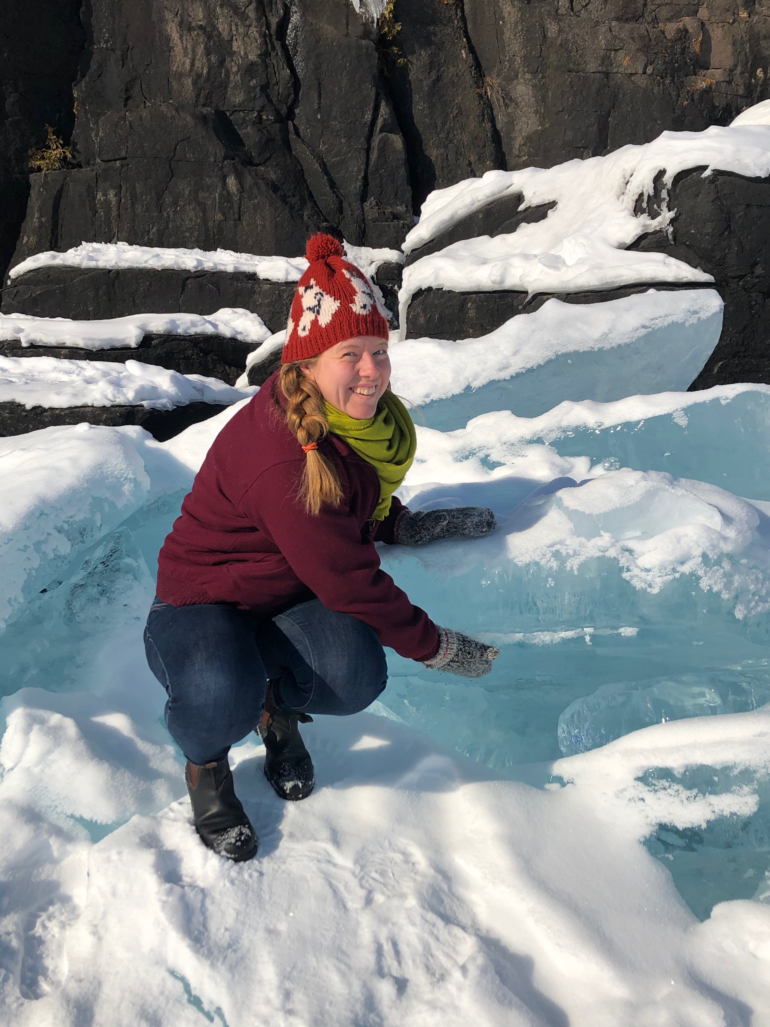 Me, a woman in a knit hat, showing the thickness of some blue ice on the shore of Lake Superior